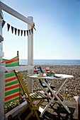 Table and chairs on terrace of beach hut on shingle beach West Sussex coastline, England, UK