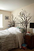 Doppelbett mit Metallkopfteil und dekoriert mit Arrangement aus Zweigen in einem Haus in Lincolnshire, England, UK