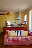 Pinkfarbenes Sofa in offener Küche mit Kücheninsel in Cromer Strandhaus, Norfolk, England, UK