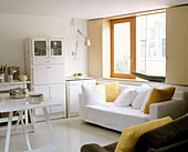 Modern sitting room area with a large window illuminating a white couch facing a table with plates piled up on