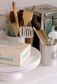 Close up detail of a box of biscuits on a cake stand next to kitchen utensils in antique storage jars