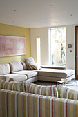 A modern sitting room towards a large L shaped sofa below a pink abstract painting next to a large window