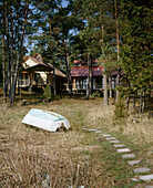 Exterior view of a traditional wooden house surrounded by trees with upturned boat next to a path leading to it