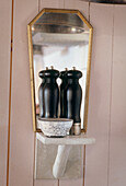 Close up of black salt and pepper pots on a ledge in front of a small mirror