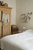 Animal horns on wall above wooden bedside table next to simple double bed with neutral cover
