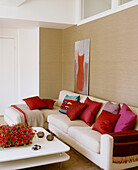 A modern sitting room with neutral colour sofa with bright pillows and low table in front of it with red flowers