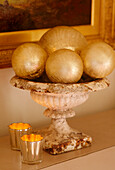 A detail of Christmas decorations gold baubles in stone urn lit candles in holders 