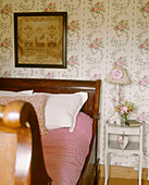 Lamp on bedside table next to wooden sleigh bed in country style bedroom