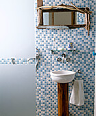 Washbasin set on wood pedestal against mosaic tiles