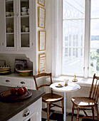 Breakfast table and wooden chairs beneath window in country style kitchen