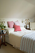 A traditional country cottage bedroom with a double bed upholstered chair two bedside tables cushions blanket throw