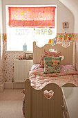 Detail eines in rosa Farben dekorierten Kinderzimmers Einzelbett mit dekorativem hölzernem Kopfteil Raffrollo am Fenster Bettdecke und Tapete mit Blumenmuster
