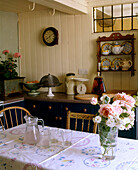 A yellow country dining room painted wood panelling table with cloth wooden chairs sideboard clock flower arrangement