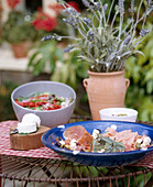 Mediterane Antipasti mit Salat, Schinken und Ziegenkäse auf Metalltisch im Garten