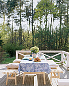 Gartentisch mit Tischtuch und Holzbänken auf einer Terrasse mit weißem Zaun