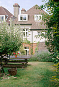 The view of the house from the back garden with a lawn and wooden bench