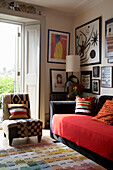 Collection of artwork displayed above black sofa with red throw