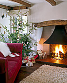 A cosy country sitting room decorated for Christmas beamed ceiling fireplace with lit fire decorated Christmas tree with presents rug upholstered sofa