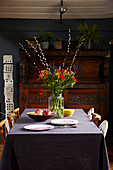 Cut flowers and pomegranates on dining table with antique wooden sideboard in Brighton home East Sussex, UK