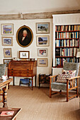 Gerahmte Bilder, Bücherregal, antike Kommode und Polsterstuhl in einem Haus aus dem 17. Jahrhundert in Hampshire, England, UK
