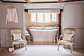 Antique chairs at entrance to open plan en suite bathroom in restored Grade II listed farmhouse Kent, UK