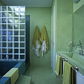 Einteiliges Waschbecken und zwei Armaturensets in Betontisch mit venezianisch gefliester Badewanne, die durch eine Glaswand aus Ziegelsteinen vom Duschbereich getrennt ist
