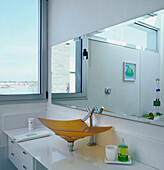 Modernes weißes Badezimmer mit großem Spiegel und Waschbecken aus farbigem Glas und Blick nach draußen