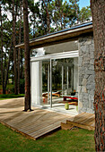 Modern glass wood and stone house in woodland setting with view into bedroom from decked veranda with sun loungers