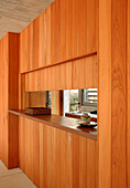 Close up of Cedar wood panelled wall between kitchen and dining area with serving hatch