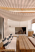 Terrace with blue and white striped cushions under canvas sheets hanging from pinewood boards