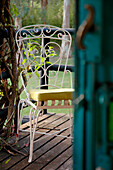 Blick durch Tür auf schmiedeeisernen weiß lackierten Stuhl auf der Gartenterrasse