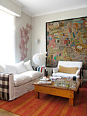 Indischer Wandteppich im Wohnzimmer mit Sofa und Kiefernholztisch auf gestreiftem Teppich