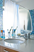 Toiletries beside washbasin and mirror reflecting shower curtain