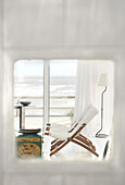 Riesige Fenster mit Blick auf das Meer, Leinenvorhänge und ein rot lackierter chinesischer Holztisch mit goldenen Motiven, Sofas und Liegestühle aus weißem Leinen