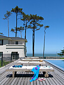 Überdachter Außenbereich am Pool eines Strandhauses mit Bäumen und Blick aufs Meer