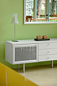 Sideboard unit set against green wall under mirror reflecting patio doors