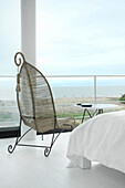 Metallgerahmter Rohrstuhl in einem weißen Schlafzimmer mit großen Fenstern und Blick aufs Meer
