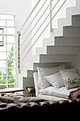 Day bed under staircase in white duplex apartment with hanging ornament on hand rail
