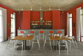 Red open plan kitchen with square shaped tables and concrete breakfast bar area
