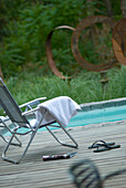 Folded towel on poolside decking with magazine and pair of flip flops