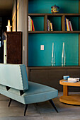 Leather upholstered two seater sofa at bookcase with vibrant turquoise painted wall