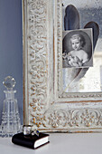 Corner of carved picture frame with glass decanter and black and white portrait picture