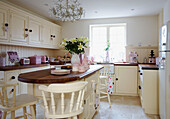 Sunlit kitchen with pink appliances and wooden island unit with painted white barstools