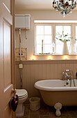 Roll top bath below sunlit window in panelled bathroom with wall mounted cistern