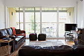 Braune Ledersofas in einem sonnendurchfluteten Wohnzimmer mit Glasschiebeverglasung, durch die die Sonne das Gebäude aufheizen kann