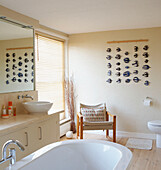 Freestanding bath in sunlit bathroom with chair at mirror and art installation