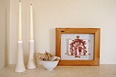 Cream candles and a bowl of dried flowers with framed artwork