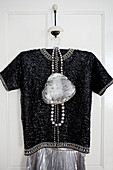 Black beaded top and silver handbag hang on back of bedroom door