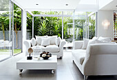 Weißes Sofa und Tisch auf Rollen in Glasanbau mit Terrassenschiebetüren