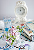 Schnittblumen, Bücher und Uhr auf einem Nachttisch in einem Cottage in Devon